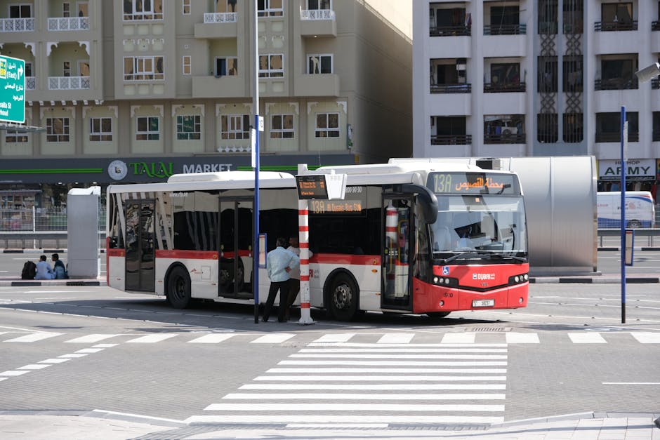 Public bus parked at a Dubai street bus stop with city buildings in the background.